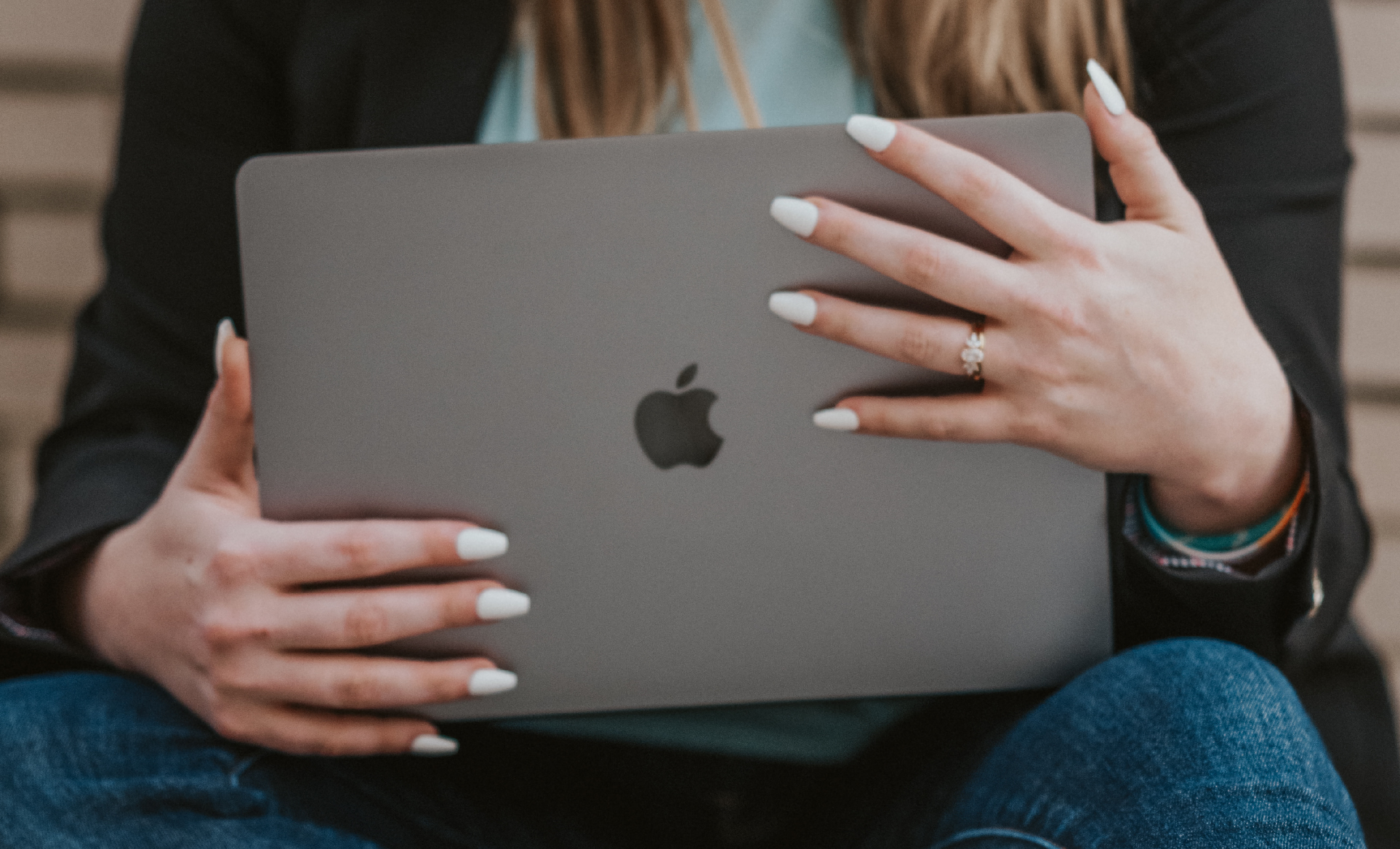 photo of a laptop being held by a woman with white nails and sitting on the ground